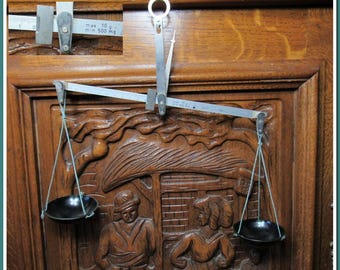 Puede incluir: Una balanza de equilibrio de plata con dos cuencos colgando de ella. La balanza está montada sobre una superficie de madera con un diseño tallado. La balanza tiene una capacidad máxima de 10 gramos y una capacidad mínima de 500 miligramos.