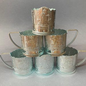 Puede incluir: Seis posavasos de metal plateado apilados. Cada posavasos presenta un diseño en relieve detallado y un asa. Los diseños detallados crean una exhibición interesante.