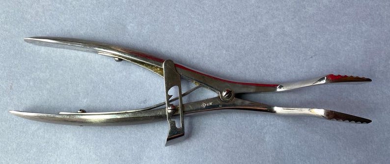 K&ouml;nnte beinhalten: Ein silberfarbenes chirurgisches Instrument mit Scharnierdesign. Das Werkzeug hat gebogene Griffe und gezahnte Spitzen. Das Instrument dient zum Klemmen oder Greifen von Objekten.