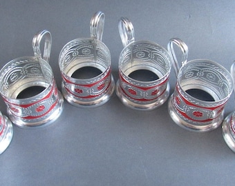 May include: Set of six silver-colored metal tea glass holders with red and white decorative patterns.