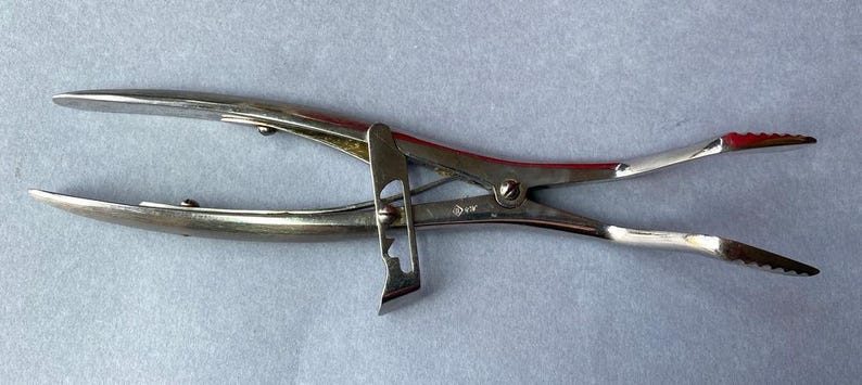 K&ouml;nnte beinhalten: Ein silberfarbenes chirurgisches Instrument mit gebogenen Backen und gezahnten Spitzen. Das Werkzeug hat ein Scharnierdesign mit einem Verriegelungsmechanismus und ist zum Greifen oder Halten von Objekten bestimmt. Das Instrument besteht aus Metall und wird wahrscheinlich in medizinischen oder wissenschaftlichen Bereichen verwendet.