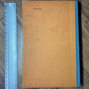 May include: A vintage book with an orange cover and a blue spine. The cover has some wear and tear, with the text "4 руб. 50 коп." printed in the upper left corner. A ruler is placed next to the book.