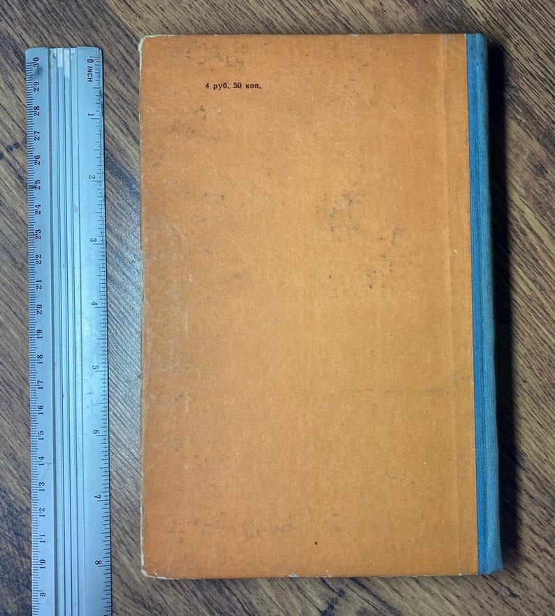 May include: A vintage book with an orange cover and a blue spine. The cover has some wear and tear, with the text "4 руб. 50 коп." printed in the upper left corner. A ruler is placed next to the book.