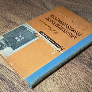 May include: A vintage book with an orange cover and blue spine, titled in Russian. The cover features an illustration of a film projector. The book's title is "Kinoteatralnye Gromkogovoriteli" and the author is listed as "M. Bogomolov".