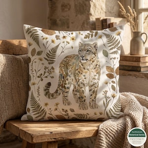 May include: Square decorative pillow featuring a snow leopard illustration. The pillow has a white background with a botanical design of ferns and flowers in shades of brown and yellow. The pillow is made of natural cotton.