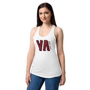 Op de afbeelding: Witte tanktop met een rood-zwart geruit "VA"-ontwerp en de tekst "EST 1947". De tanktop heeft een racerback-ontwerp en is gemaakt van een zacht materiaal. Het model draagt een blauwe spijkerbroek.