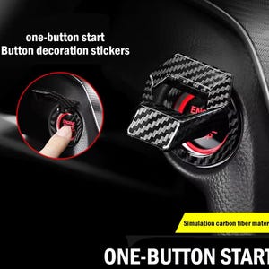 Op de afbeelding: Zwarte en zilveren koolstofvezel knopdecoratiestickers voor de ontsteking van een auto. De stickers zijn ontworpen om het uiterlijk van het one-button startsysteem te verbeteren. De tekst "ONE-BUTTON START" is ook zichtbaar.