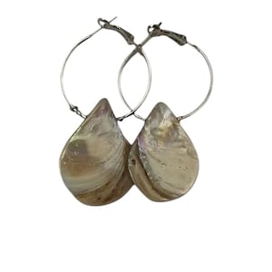 May include: A pair of silver hoop earrings with iridescent, teardrop-shaped pendants. The pendants have a pearlescent, shell-like appearance, reflecting a range of colors. The earrings are set against a white background.