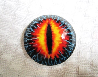 May include: A round, glass eye with a red and yellow iris and a black pupil. The eye is surrounded by a blue and black border with a lightning bolt pattern.