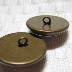 Peut inclure: Deux boutons en m&eacute;tal couleur or avec une boucle sur le dessus. Les boutons sont ronds et ont une surface lisse.
