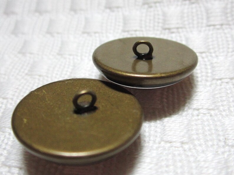 Peut inclure: Deux boutons en m&eacute;tal couleur or avec une boucle sur le dessus. Les boutons sont ronds et ont une surface lisse.
