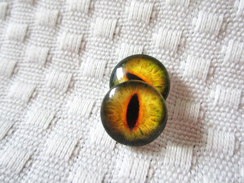 May include: Two round, yellow and green glass eyes with black pupils. The eyes are on a white textured surface.
