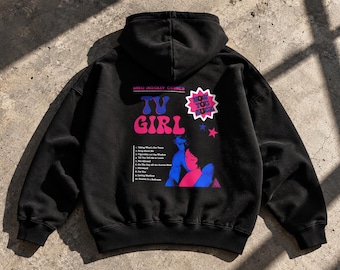 May include: A black hooded sweatshirt featuring a graphic on the back with the text "WHO REALLY COMES", "TV GIRL", and "HOW YOU SURF". The design includes a tracklist of ten songs and a stylized illustration of two figures in blue and pink.