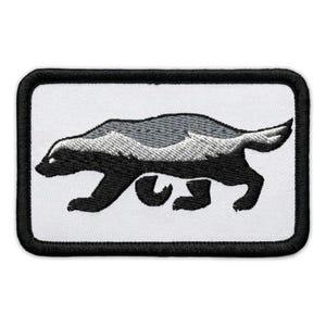 May include: Embroidered patch featuring a black and white badger in a walking pose. The badger has a gray back and a white belly, with a black outline and border. The patch is rectangular.