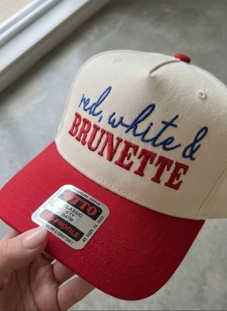 Peut inclure: Casquette de baseball avec une visi&egrave;re et un bouton rouges, et une couronne cr&egrave;me. Le chapeau porte la broderie "red, white & BRUNETTE" en rouge et bleu. Un autocollant est visible sur la visi&egrave;re.