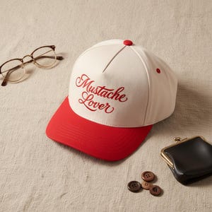 May include: A white and red baseball cap with the text "Mustache Lover" in red script. The cap has a red brim and a red button on top. Also pictured are eyeglasses, a small black coin purse, and several brown buttons.