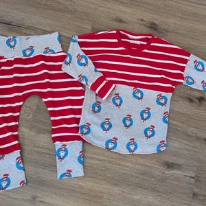 Könnte beinhalten: Ein rot-weiß gestreiftes Langarmshirt und eine passende Hose. Das Shirt hat rot-weiße Streifen auf der Oberseite und grauen Stoff mit einem Cartoon-Charakter-Aufdruck auf der Unterseite. Die Hose ist rot-weiß gestreift mit grauen Bündchen.