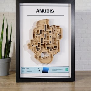 Puede incluir: Obra de arte enmarcada que presenta un mapa tridimensional detallado del nivel de juego Anubis. El mapa es de color marrón claro y está sobre un fondo blanco, con la palabra "ANUBIS" en la parte superior. El marco es negro.