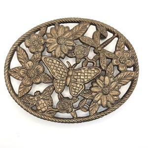 May include: Oval-shaped, bronze-colored metal decorative piece featuring a butterfly, flowers, leaves, a dragonfly, and a bee. The design is openwork, with a rope-like border. The butterfly has a checkered pattern on its wings.