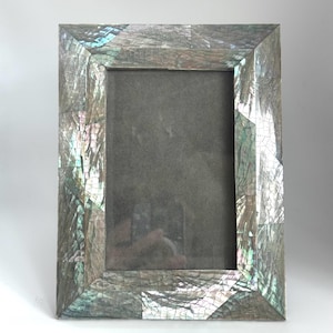May include: Rectangular photo frame with a mosaic-like design. The frame is primarily gray with iridescent accents of blue, green, and pink. The frame's surface has a cracked, textured appearance. The inner area is a dark gray color.