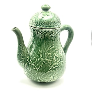 May include: A green ceramic teapot with a lid, spout, and handle. The teapot is decorated with a leaf pattern and has a glossy finish. The teapot is a decorative item for the kitchen or dining room.