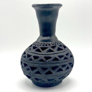 May include: A black ceramic vase with a bulbous body and a slender neck. The vase features intricate cut-out geometric patterns around the body, creating a textured surface. The vase is approximately 7 inches tall.