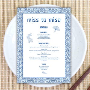 Pode incluir: Um menu de sushi intitulado "miss to miso" com uma borda azul ondulada e ilustrações de um peixe e um leque. O menu está em um prato branco com pauzinhos em um tapete de bambu.