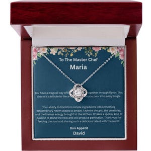 May include: A silver necklace with a four-leaf clover pendant, presented in a wooden gift box. The box contains a card with text that reads "To The Master Chef Maria" and a message. The box is lined with white satin.