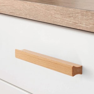 May include: A light-coloured wooden cabinet pull handle. The handle is rectangular with a curved edge and is mounted on a white cabinet door. Various sizes are shown in millimetres.