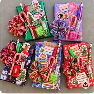 May include: Five rectangular gift-wrapped packages featuring holiday themes, each adorned with a colorful scrunchie, a candy cane, a pencil, a small pencil sharpener, a tube of beads, sticky notes, and various Christmas-themed stickers.