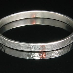 May include: A silver hammered bangle bracelet. The bracelet is smooth and shiny, with a hammered texture.