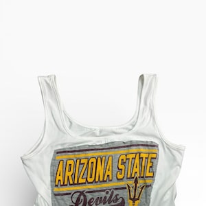 May include: A white ceramic mug with a black handle and the text "But First, Coffee" in a bold, black font. The mug is filled with a dark liquid, likely coffee, and sits on a light-colored surface.