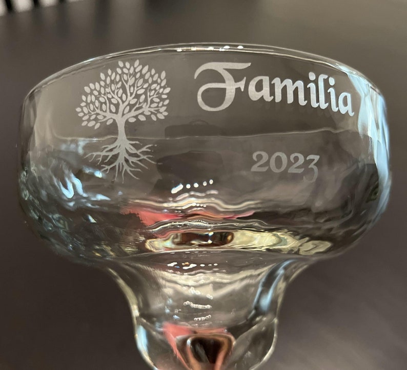 K&ouml;nnte beinhalten: Ein klares Glas-Margarita-Glas mit einem gravierten Design eines Baumes mit Wurzeln und dem Wort "Familia" und dem Jahr "2023" am Rand.