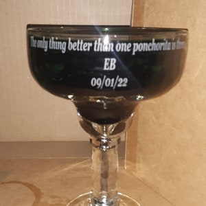 K&ouml;nnte beinhalten: Ein schwarzes Margarita-Glas mit dem Text "The only thing better than one ponchoria is three" und "EB 09/01/22" auf der Seite.