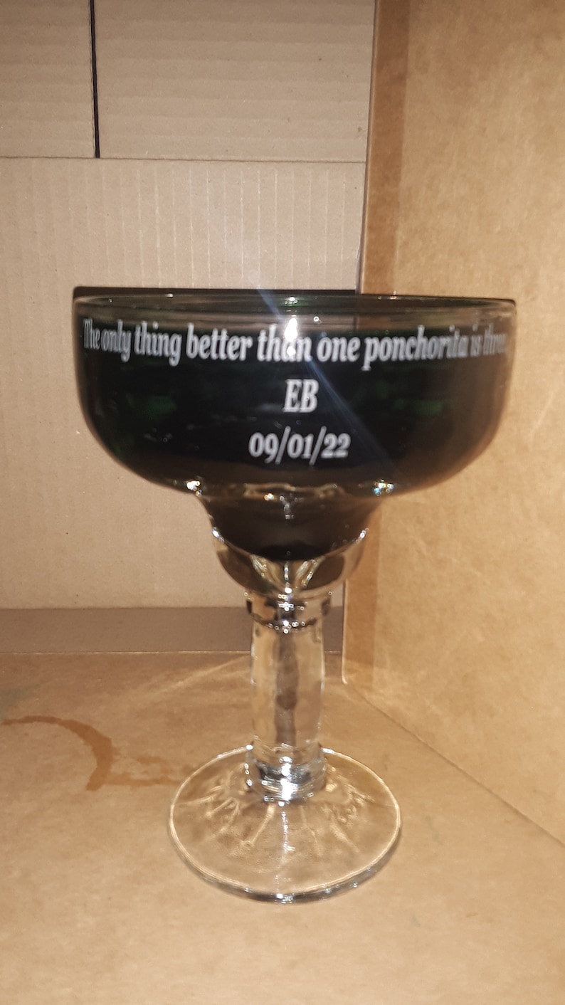K&ouml;nnte beinhalten: Ein schwarzes Margarita-Glas mit dem Text "The only thing better than one ponchoria is three" und "EB 09/01/22" auf der Seite.