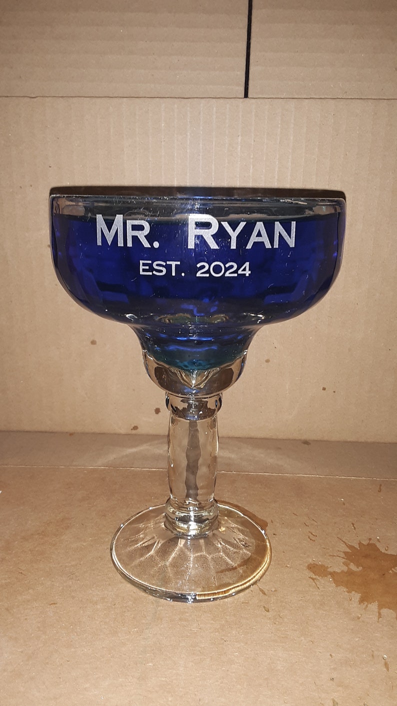 K&ouml;nnte beinhalten: Ein blaues Glas-Margarita-Glas mit dem Text "MR. RYAN EST. 2024" auf der Seite.