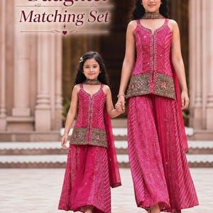 May include: A mother and daughter matching set in a vibrant pink hue. The outfits feature intricate embroidery and a flowing skirt design. The image includes the text "Mother & Daughter Matching Set".