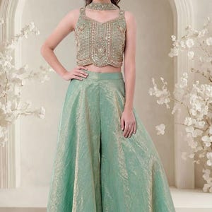 May include: A sage green two-piece outfit consisting of a sleeveless, cropped bodice with intricate gold embroidery, beadwork, and a high neck collar, paired with matching wide-leg, floor-length trousers featuring a subtle metallic sheen.