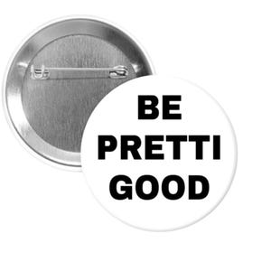 May include: A white button with the text "BE PRETTI GOOD" in black, with a silver pin back. The button is round and has a simple, clean design. The button is a fun accessory.