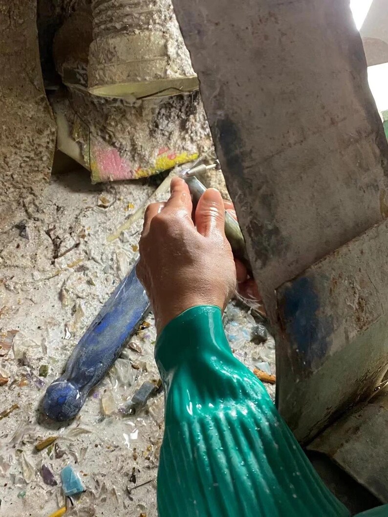 Puede incluir: Una persona con un guante verde utiliza una herramienta para trabajar en una piedra. La piedra est&aacute; rodeada de escombros. Un objeto azul est&aacute; en el fondo.