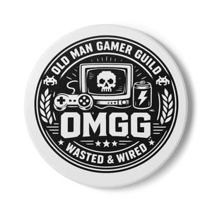May include: A white, circular button with a black graphic design. The design features a retro video game theme with a skull on a screen, a joystick, and the text "OLD MAN GAMER GUILD" and "OMGG WASTED & WIRED".