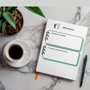 K&ouml;nnte beinhalten: Ein wei&szlig;es Notizbuch mit dem Wort "Affirmations" und zwei Beispielen f&uuml;r Affirmationen. Eine Tasse Kaffee, ein Stift und eine Topfpflanze befinden sich ebenfalls auf der Marmoroberfl&auml;che.