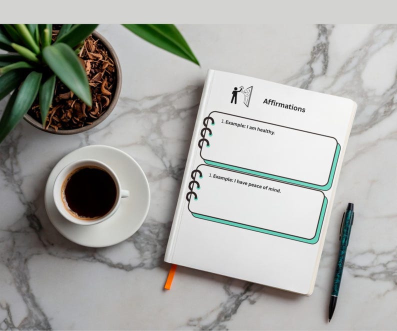 K&ouml;nnte beinhalten: Ein wei&szlig;es Notizbuch mit dem Wort "Affirmations" und zwei Beispielen f&uuml;r Affirmationen. Eine Tasse Kaffee, ein Stift und eine Topfpflanze befinden sich ebenfalls auf der Marmoroberfl&auml;che.