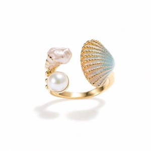 May include: A gold ring with a seashell design. The ring features a large, pearlescent white pearl and a seashell with blue and gold detailing. The ring's design is inspired by the ocean and marine life.
