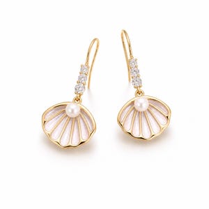 Peut inclure: Une paire de boucles d'oreilles en forme de coquillage dorées. Chaque boucle d'oreille présente un motif de coquillage blanc et doré avec une perle au centre. Trois petites pierres transparentes sont serties au-dessus de la coquille.