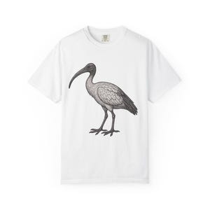 Peut inclure: T-shirt blanc avec une illustration détaillée en noir et blanc d'un oiseau au long bec courbé. L'oiseau est représenté dans des tons de gris et de noir, debout sur deux pattes. Le t-shirt a un col rond et des manches courtes.