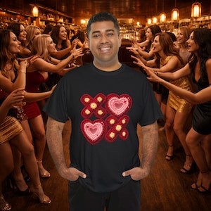 Puede incluir: Camiseta negra con un diseño de corazones rojos y detalles florales amarillos. El diseño es una combinación de ganchillo y bordado. La camiseta la lleva una persona en un bar.