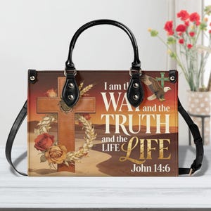 May include: A brown leather handbag with a black handle and strap. The bag features a cross, roses, and text that reads "I am the Way, the Truth, and the Life, John 14:6." An eagle graphic is also present.