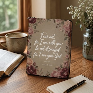 May include: A rectangular book cover with a muted taupe background, decorated with dark pink and mauve floral patterns at the corners. The text reads: Fear not, for I am with you; be not dismayed, for I am your God. ISAIAH 41:10 is printed below.