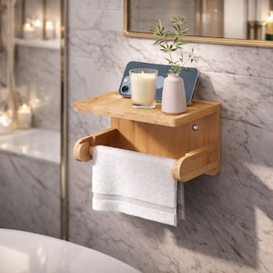 May include: A bamboo bathroom shelf and towel rack combination. The shelf holds a lit candle, a smartphone, and a small vase with greenery. A white towel hangs from the rack below. The fixture is mounted on a marble wall.
